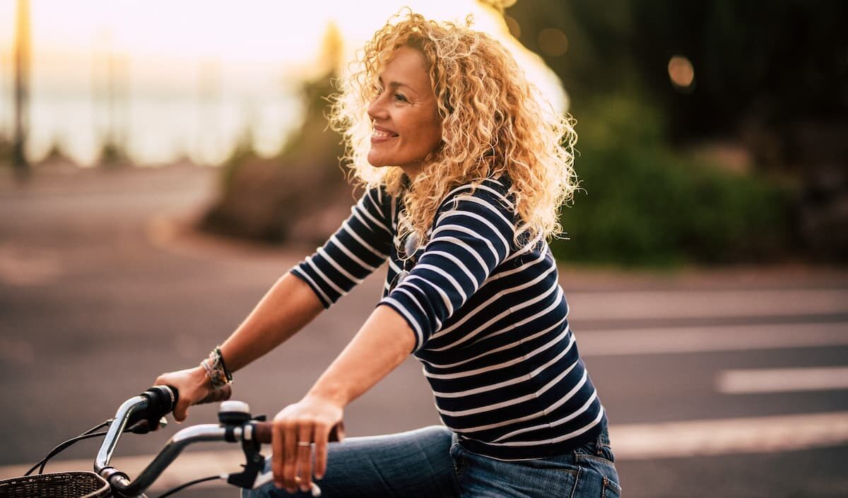 Cheerful blonde curly woman smile and enjoy the ride on a bike in outdoor leisure activity in the city