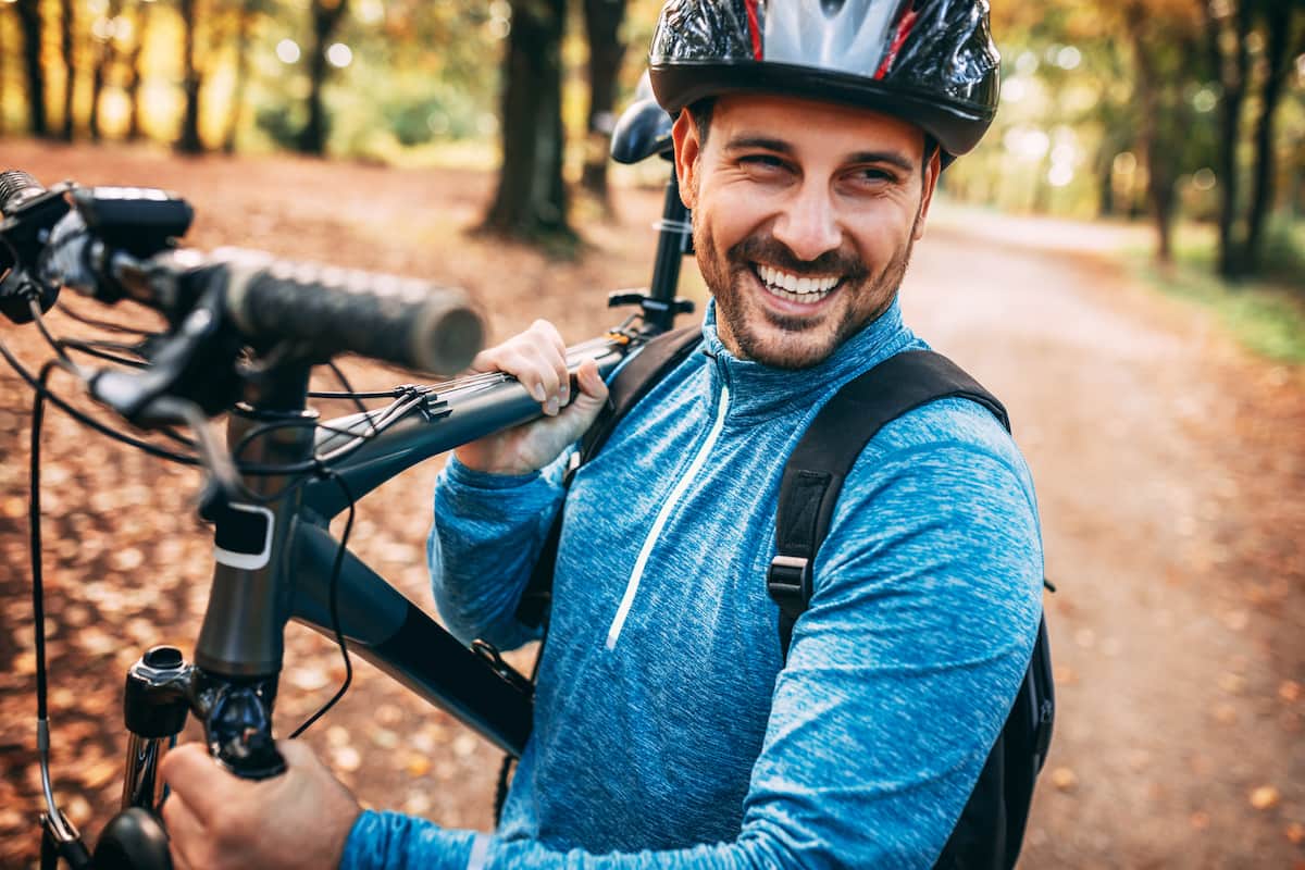 Young athletic man standing with bicycle in autumn park.
