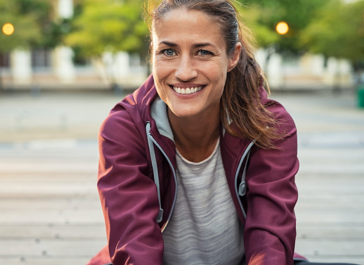 Portrait of smiling woman sitting on floor of city street after running
