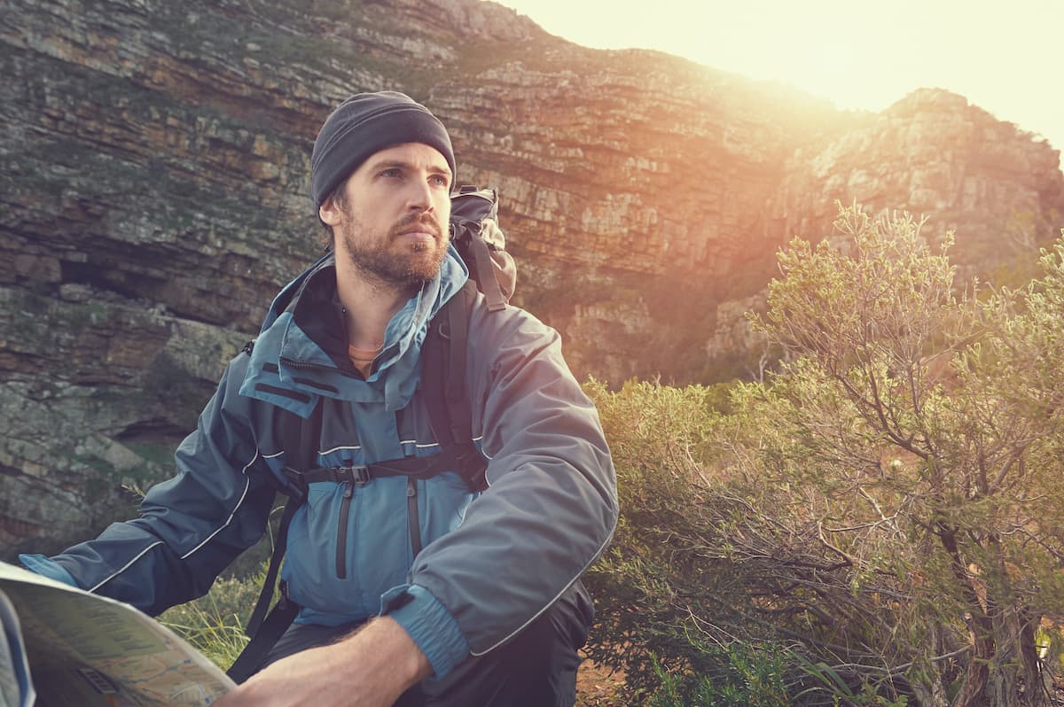 portrait of adventure man with map and extreme explorer gear on mountain with sunrise or sunset