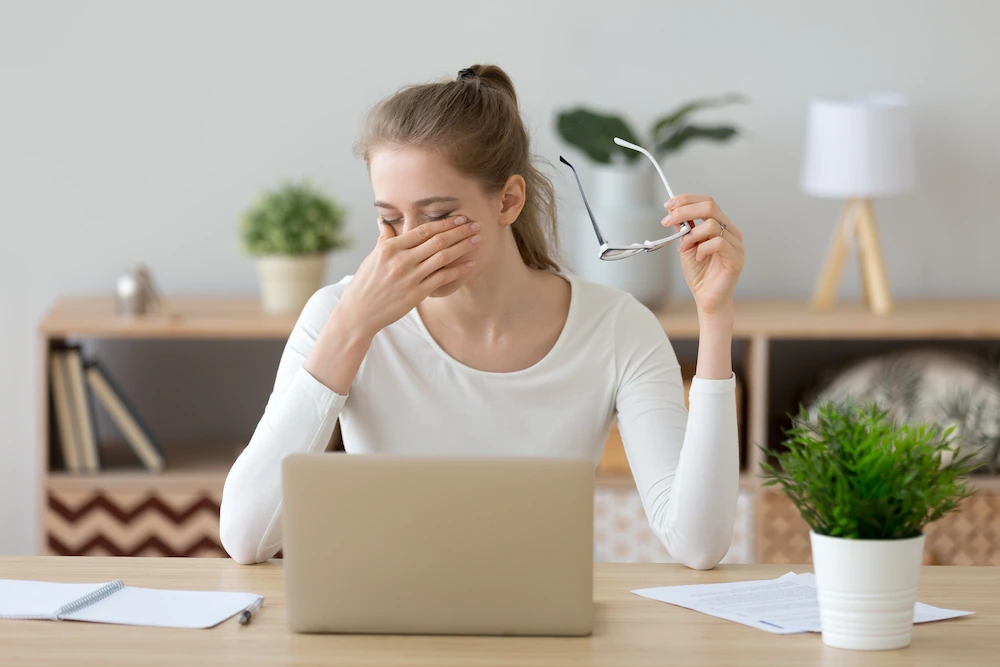 Young woman rubbing her eyes while working on her laptop
